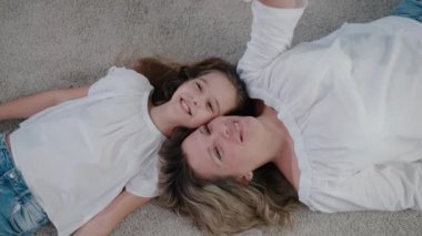 Güzel bir anne ve kız evin içinde yerde yatar ve yukarı bakar, gülümser ve sohbet eder. Üst görünüm