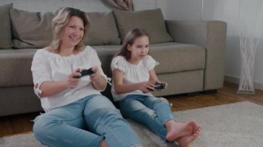 Komik anne ve kızı itişip kakışarak gülüyor ve konsol bilgisayar oyunu oynuyorlar. Kız kazanır ve zevkle ellerini havaya kaldırır. Yavaş çekim
