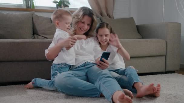 Щаслива кавказька родина мама і мила маленька дочка і син сміються використовувати смартфон онлайн дистанція розмовляти смішне обличчя і посміхатися повільний рух — стокове відео