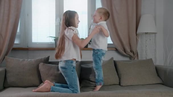 Filhos felizes de irmão bonito e irmã menina e menino pulando no sofá enquanto se divertem durante a manhã em férias em casa juntos — Vídeo de Stock