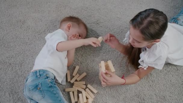 Chica y niño caucásicos jugando jenga en casa en un día soleado brillante, riendo y divirtiéndose juntos. Ángulo de vista — Vídeo de stock