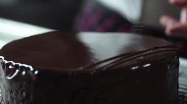 Şef tatlı olarak kremalı bir çikolatalı pasta hazırlar, yüzeyi şekerleme konisiyle süslenir.