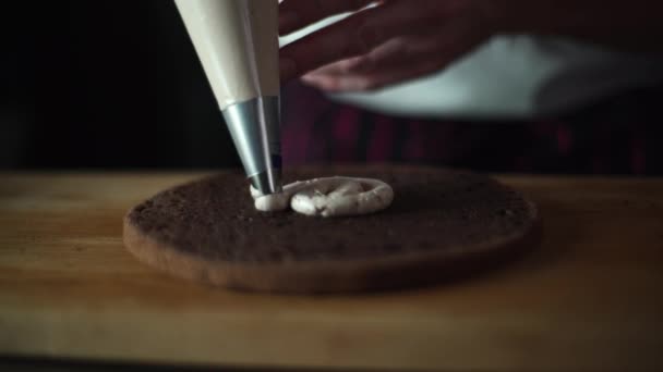 Bakverk kocken pressar grädden från röret på tårta lagret i en cirkulär rörelse i en spiral — Stockvideo