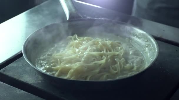 The chef puts the pasta into the skillet with a creamy sauce to prepare carbonara with tongs Stock Video