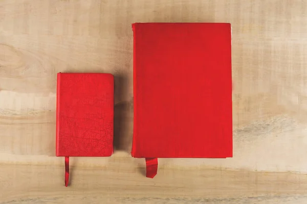 Two books of red color lie on a wooden table