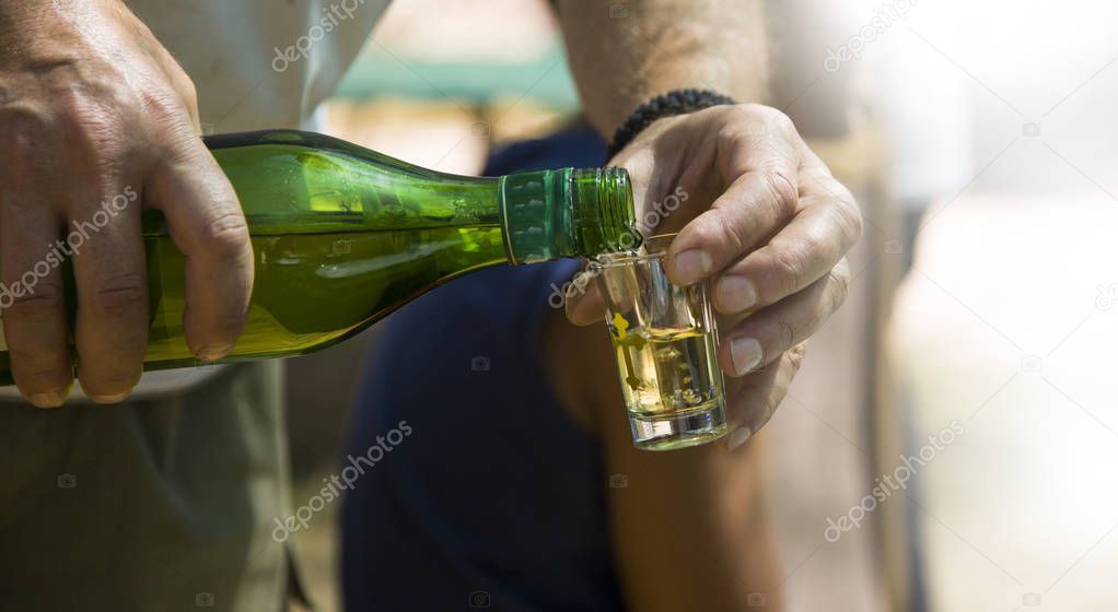 the host pours homemade brandy into a small bottle,Hand pours a 