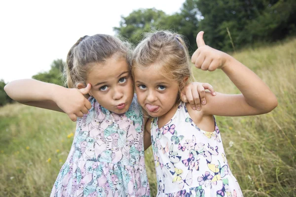 Two sisters playing - with one hand covers mouth of another, aga