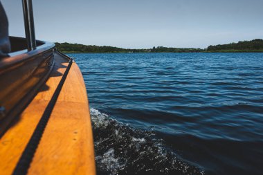 Norfolk Hatunları 'ndan geçen ahşap bir tekne. Teknenin altında suyla sulanan. Ufukta açık mavi gökyüzünün altında ağaçlar görülebilir..