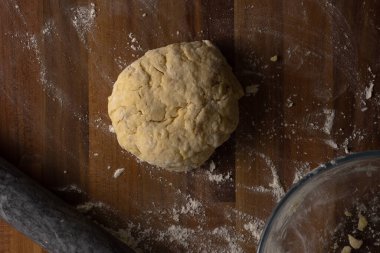Peynirli çöreğin üst görüntüsü ahşap bir yüzeyde yuvarlanmış bir top, yuvarlak bir iğne ve temiz bir cam kase ile çevrili.