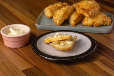 Pembe bir tereyağlı tabak ve içinde peynirli çörekler olan mavi bir tabakla çevrili bir tabakta oturan peynirli çörekler.