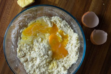 Üstünde un, yumurta, tereyağı ve peynir olan açık bir kâse. Tepeden aşağıya yumurta kabukları ve peynir ile kâsenin etrafını sarmış.