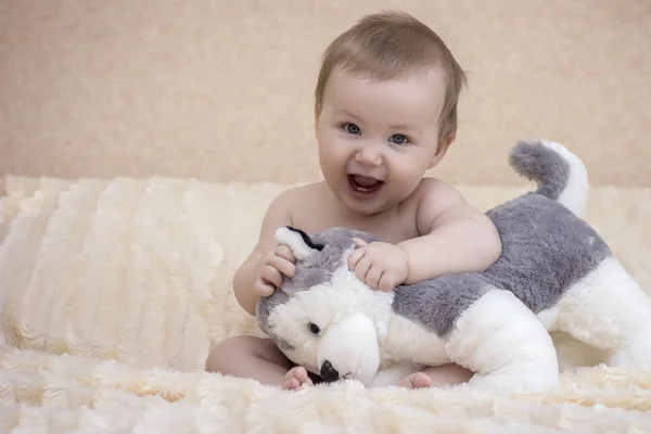 Bebelușul stă pe pat cu un câine de jucărie — Fotografie, imagine de stoc