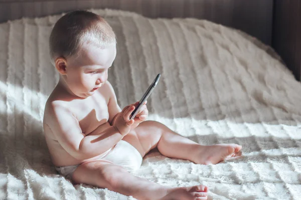 Bebé con el teléfono sentado en la cama — Foto de Stock