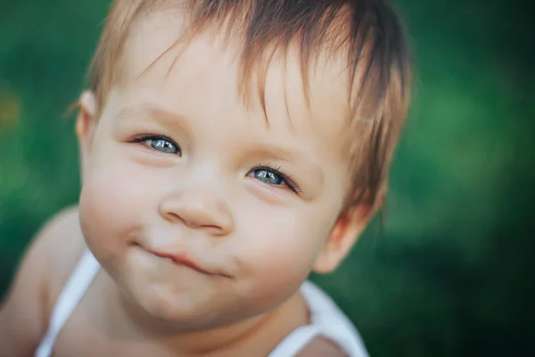 Μικρό κοριτσάκι χαμογελά με μπλε μάτια στο γρασίδι, κοντινό πλάνο — Φωτογραφία Αρχείου