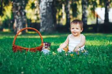 Sepet yakınındaki çimenlerin üzerinde oturan gülümseyen bebek kız