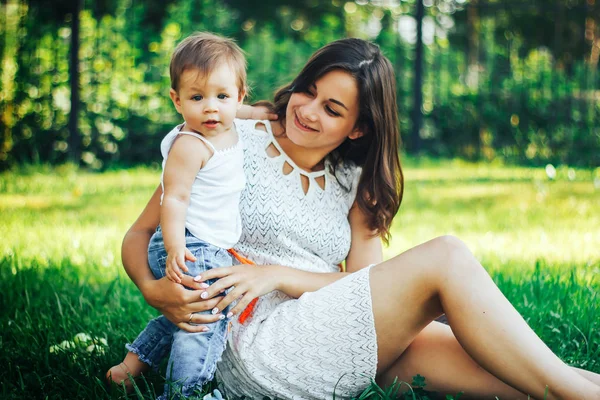 Mutlu anne bebeği ile çimlerde oturan