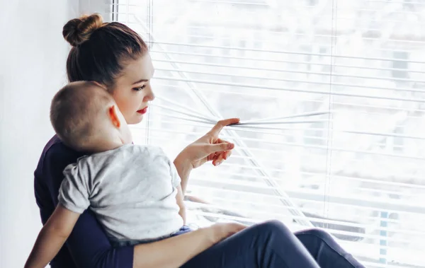 Üzgün anne bebeği ile pencere kenarında oturup, pencereden dışarı bakarak ve bir şeyler bekliyor. Bebek annemin omzuna yalan söylüyor.