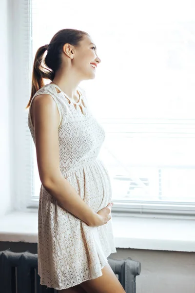 Embarazo, descanso, personas y concepto de expectativa - primer plano de la feliz mujer embarazada sonriente tocando su vientre en casa — Foto de Stock
