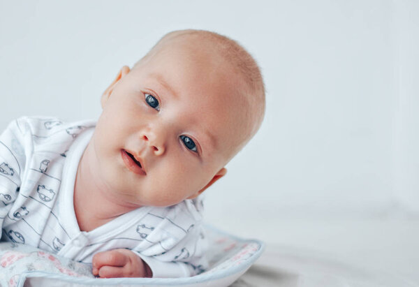 A funny baby with beautiful eyes lies on his stomach and smiles.