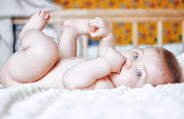 Nettes Baby mit offenen blauen Augen, das mit seinen Füßen auf dem Rücken spielt — Stockfoto