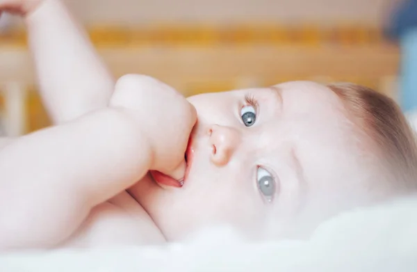 Bonito bebé con los ojos azules abiertos jugando con los pies acostados en la espalda, de cerca —  Fotos de Stock