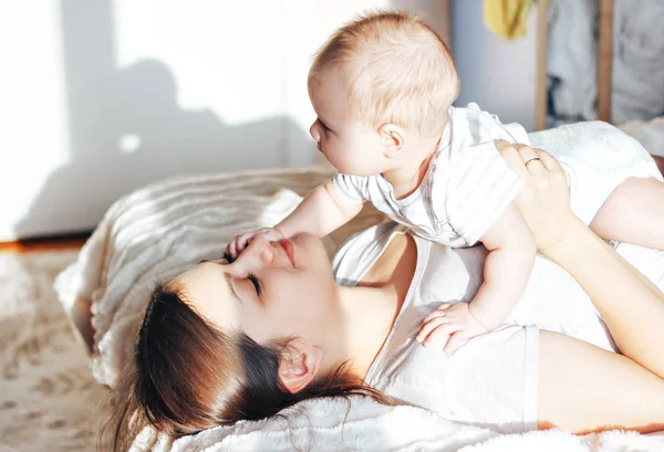 Yatağa bebeği ile oynarken, gülen genç anne — Stok fotoğraf