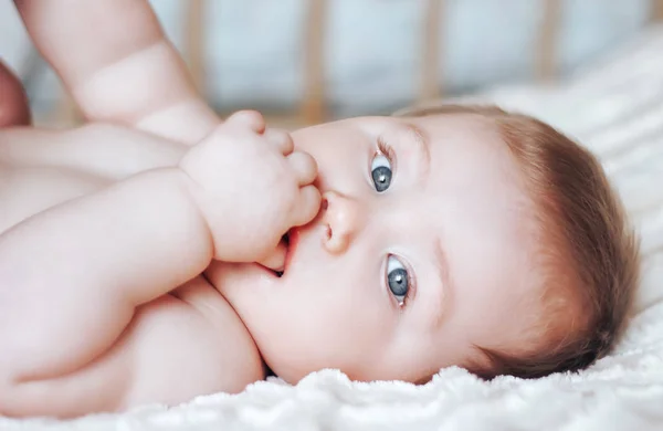 Bel bambino con gli occhi azzurri aperti che gioca con i piedi sdraiati sulla schiena, da vicino — Foto Stock