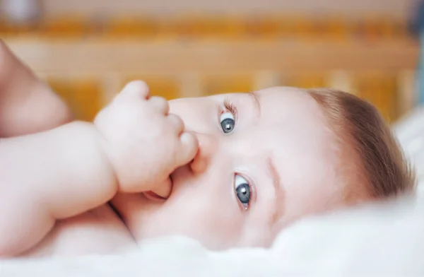 Bel bambino con gli occhi azzurri aperti che gioca con i piedi sdraiati sulla schiena, da vicino — Foto Stock