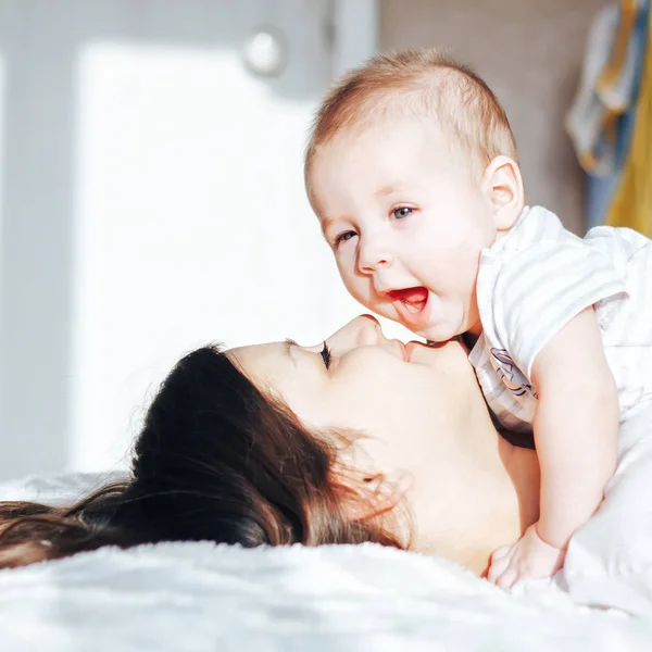 Yatağa bebeği ile oynarken, gülen genç anne — Stok fotoğraf