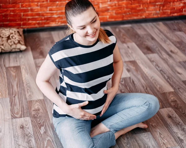 Беременная женщина сидит на полу дома — стоковое фото