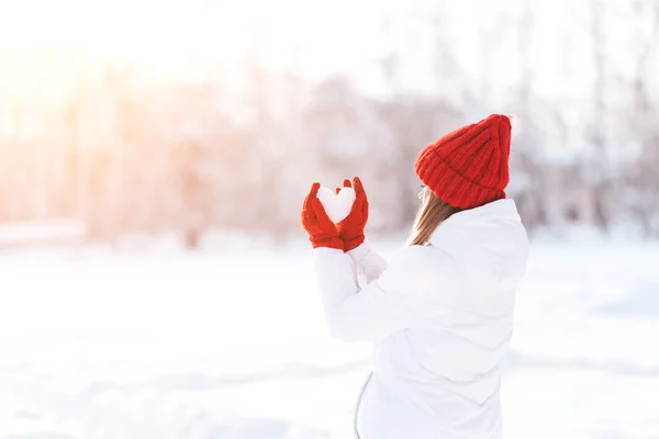 Woman in red gloves and hat holding heart shape from snow