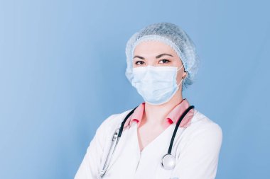 Mavi arka planda steteskopu olan maske takmış genç bir kadın doktor.