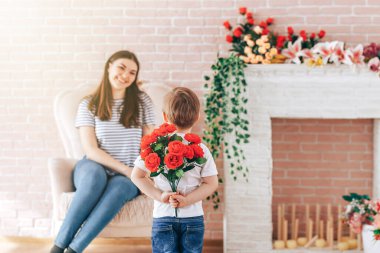 Arkasında bir buket çiçek tutan bir çocuk.