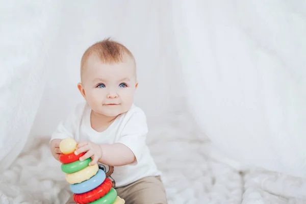 Little cute baby girl z piramidy zabawki siedzi w białym wnętrzu w domu. — Zdjęcie stockowe