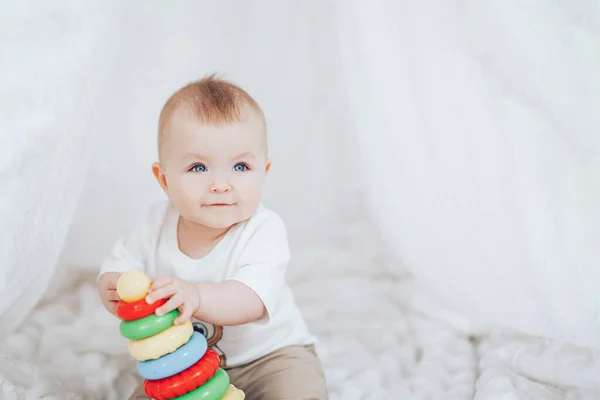 Petite fille mignonne avec une pyramide de jouets assis à l'intérieur blanc à la maison . — Photo