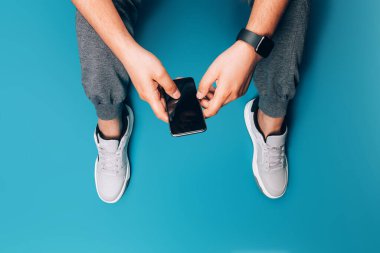 Genç adam elinde akıllı bir telefonla yerde oturuyor, telefonla yazışıyor, internette arama yapıyor, e-kitap okuyor.