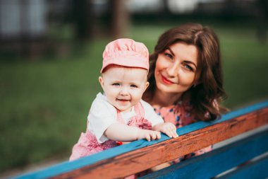 Pembe elbiselerle parkta bankta oturan küçük bir çocuğu olan güzel bir anne..