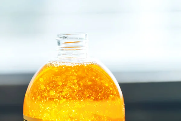 Liquid soap of orange color in a transparent bottle on a light background, liquid soap with bubbles