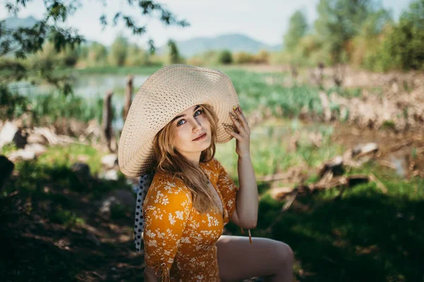 Güzel sarı elbiseli ve şapkalı güzel bir kız açık havada yeşil çimlerde oturuyor. — Stok fotoğraf