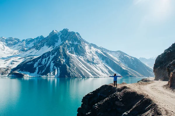 Kolları açık genç bir kadın kameraya bakıyor ve And Dağları 'ndaki El Yeso Barajı manzarasının tadını çıkarıyor..