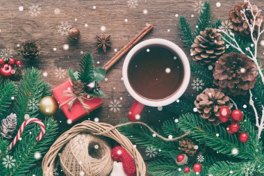 Tahta kalas, çam yaprağı, kozalak, kutsal toplar, şeker kamışı ve kırmızı bardak çikolatayı Noel konseptine göre dekore eder. Üst görünümde ahşap zemin karlı ve noel duvar kâğıdı için kopyalama alanı olan daire.