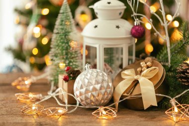 Beyaz fenerli bir Noel arkaplanı, altın hediye kutusu, şirin bir top, yıldız şeklinde sinyal lambası, ahşap masa üzerinde fotokopi alanı olan çam yaprakları ve koniler. Xmas kutlaması için Bokeh Noel ağacı duvar kağıdı.