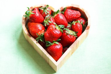 Taze olgun çilekler, kalp şeklinde ahşap bir kasede. Yaklaş.       