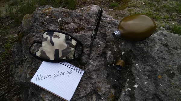 Old, army canteen for water, a knife and a medical  mask. Military flask, surviving.  Concept, quote is never give up.