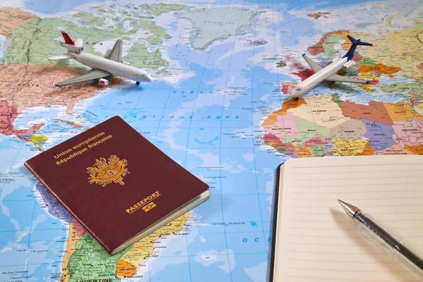 世界地图 上面有两架玩具飞机 一本法国护照和一支圆珠笔在一个开着的记事本的顶部 — 图库照片