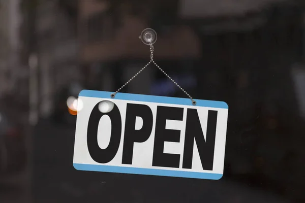 Close-up on a blue open sign in the window of a shop displaying the message \