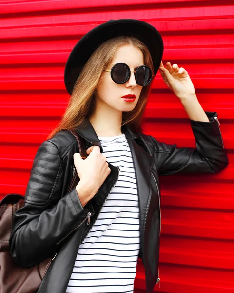 Portrait stylish young woman in black rock style stands over red — Stockfoto
