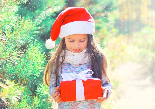 Criança de Natal menina em santa chapéu vermelho com caixa de presente perto — Fotografia de Stock