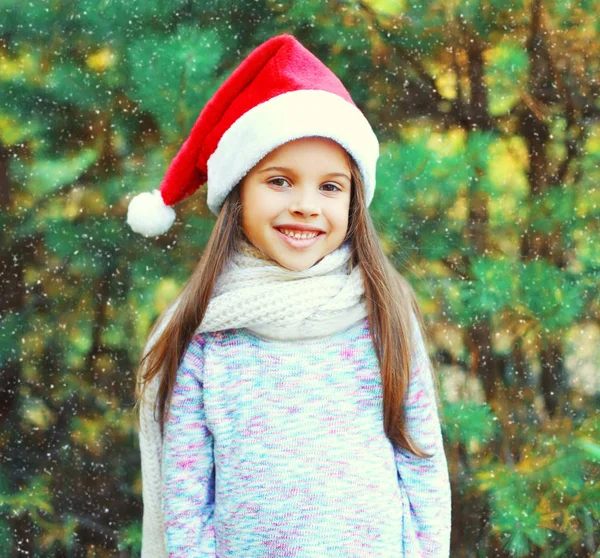 Christmas smiling child little girl in santa red hat over a tree — Stock Photo, Image