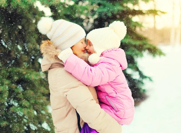 Зимняя счастливая мать обнимает ребенка за елкой и снегопадом — стоковое фото